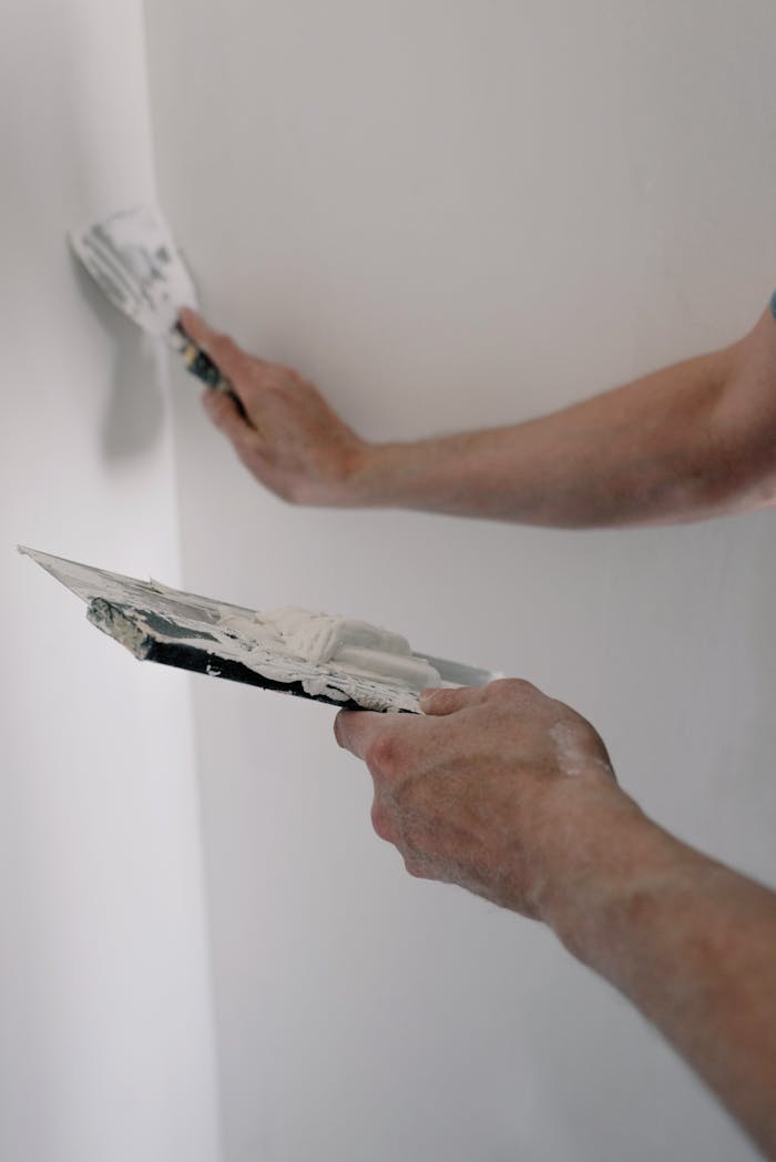 Home Hands apply spackling paste on a wall using tools, capturing a DIY renovation scene.
